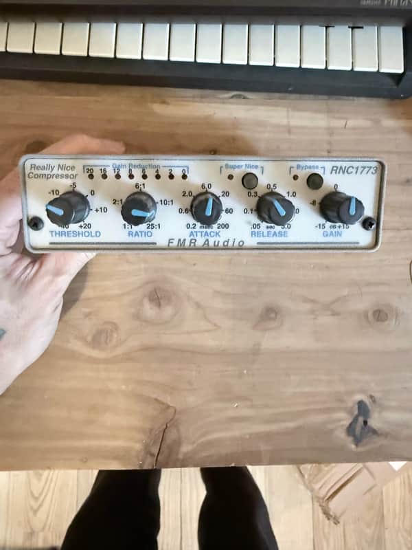 Black audio compressor unit with knobs, connected to a black cable.