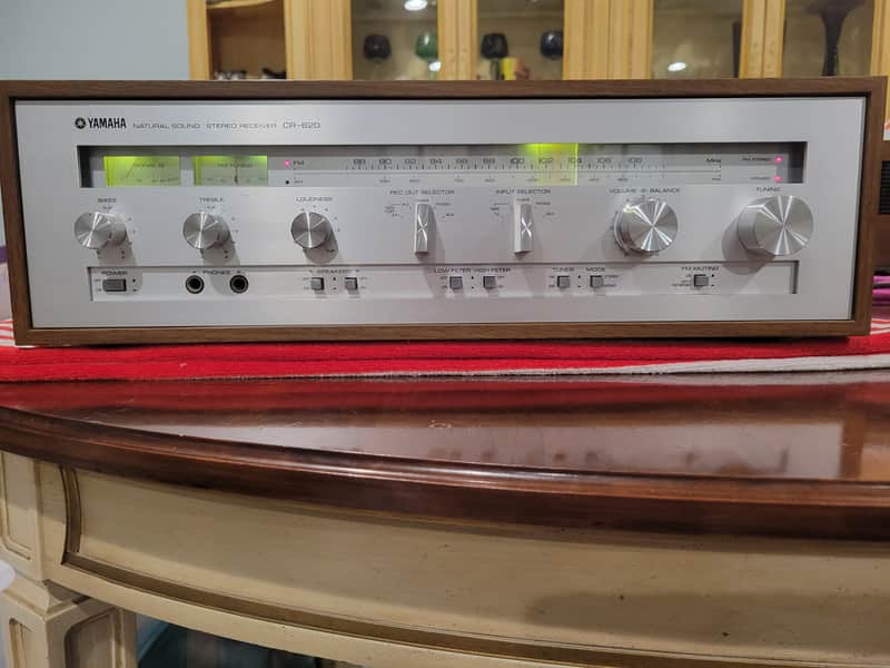 Yamaha stereo receiver, silver and black faceplate, on wooden furniture.