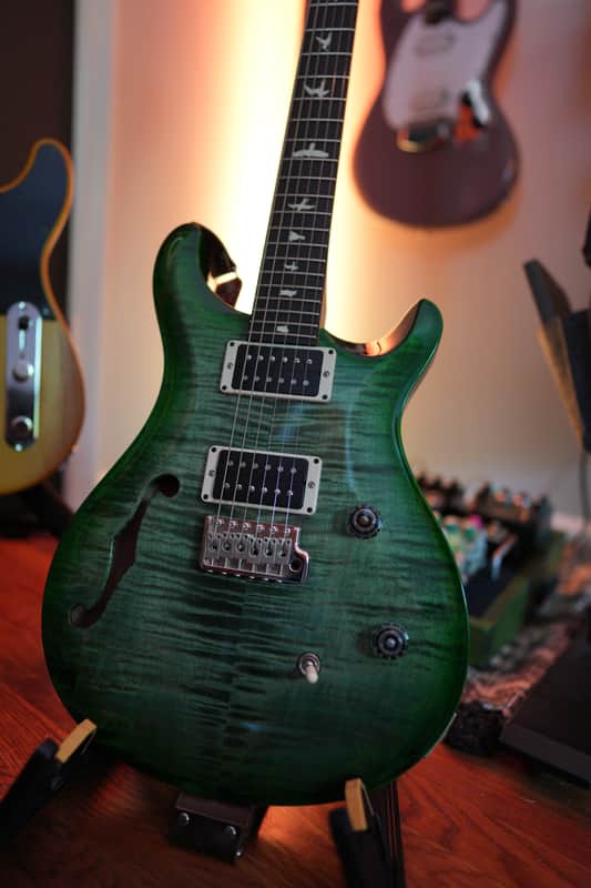 Dark wood electric guitar with black hardware, displayed against wood paneling.