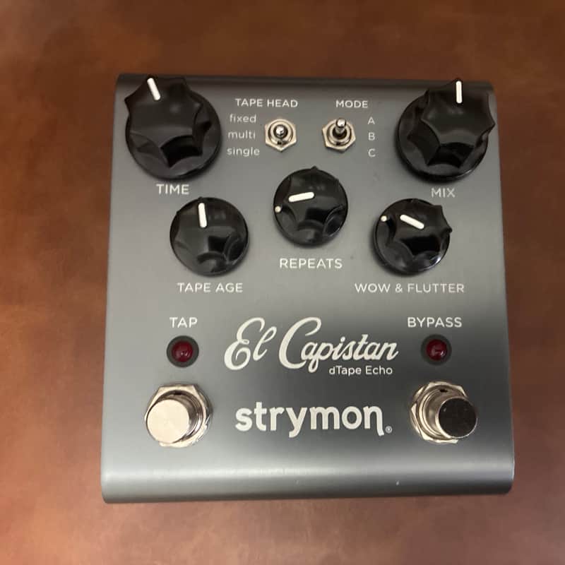 Grey stompbox with black knobs and switches, resting on green fabric.