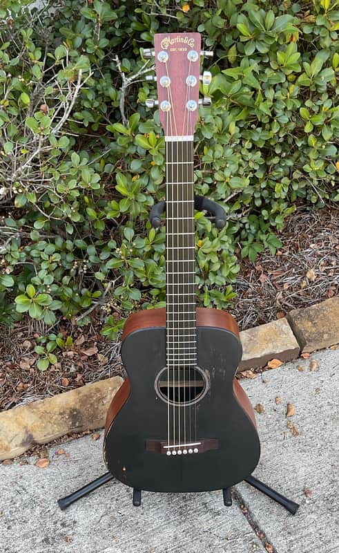 A natural wood acoustic guitar hanging against a wood-paneled background.