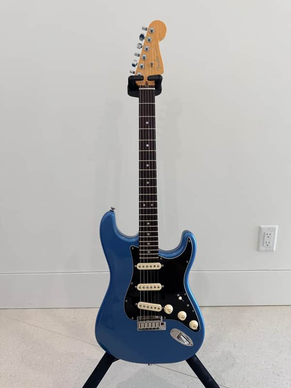 Light blue electric guitar with dark, speckled body design, resting on gray sofa.