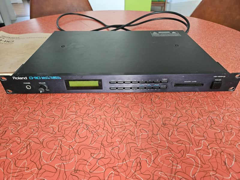 Black Roland D-110 synthesizer with cables resting on a brown surface.