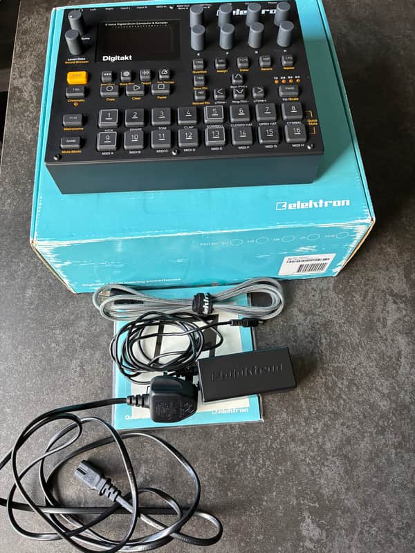 Black digital keyboard, cables, power adapter, and brown box on a wooden surface.