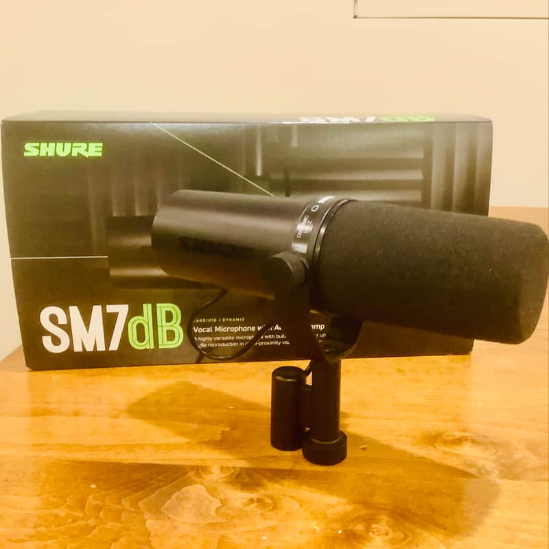 Two black Shure microphones with black foam windscreens on a wooden surface.