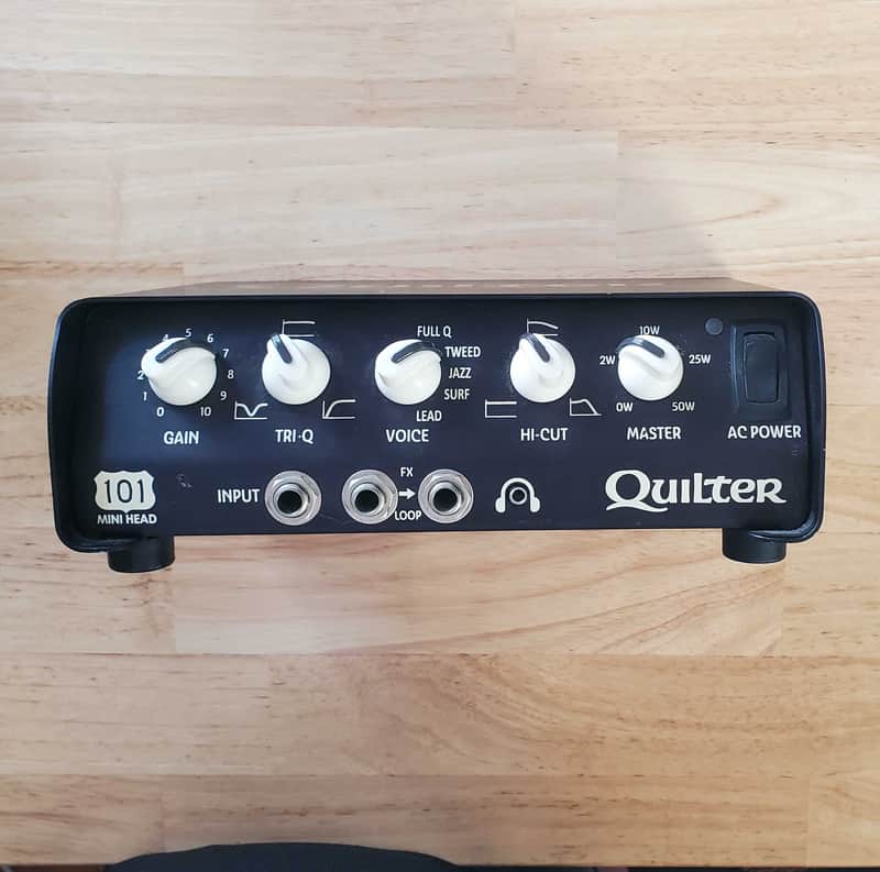 Black Quilter audio amplifier with knobs, sitting on a reflective surface.