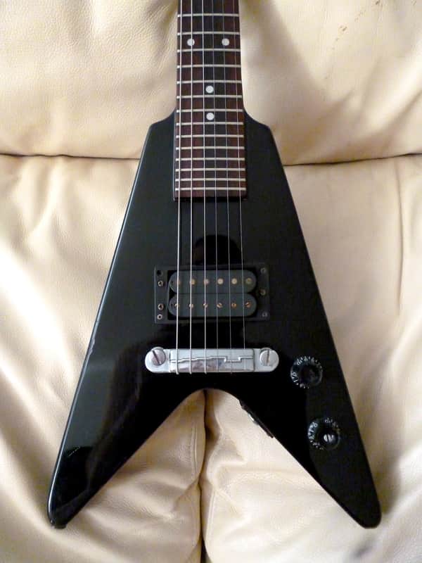 Red and white electric guitar with black hardware, resting on patterned carpet.