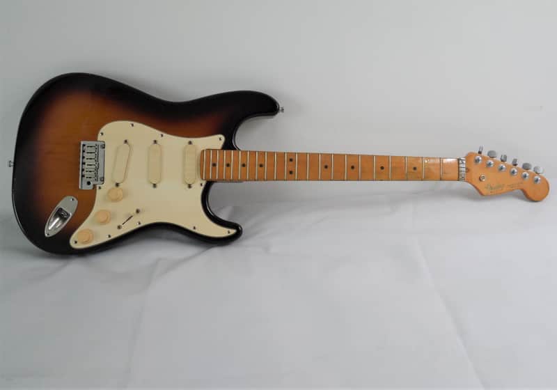 Orange and white electric guitar, standing upright, against a backdrop of amplifiers.