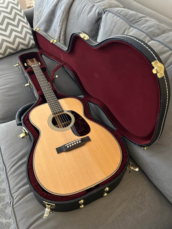 A natural wood acoustic guitar on a stand against a dark wood dresser.