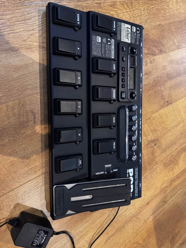 Black guitar effects pedalboard with manual controls and black instruction booklet.
