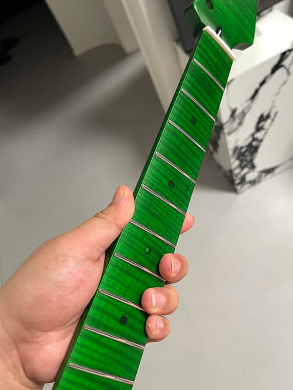 Wooden guitar neck with fretboard and inlays held by a hand.