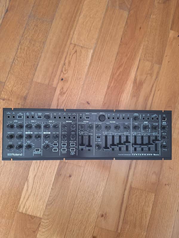 Black electronic synthesizer with numerous knobs, sliders, and labeled controls.