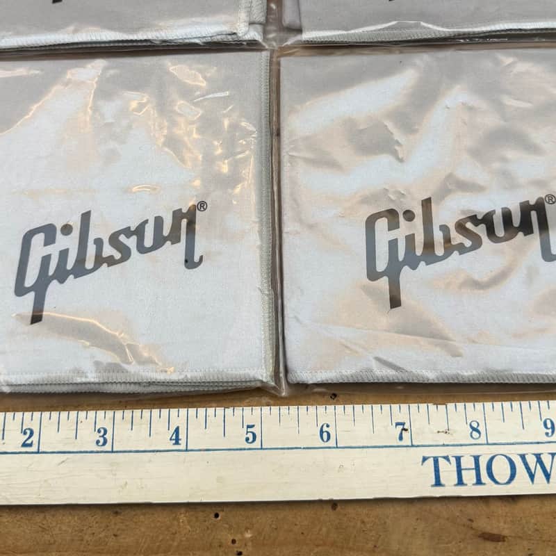 Four white Gibson logo patches displayed on a wooden surface with a ruler.