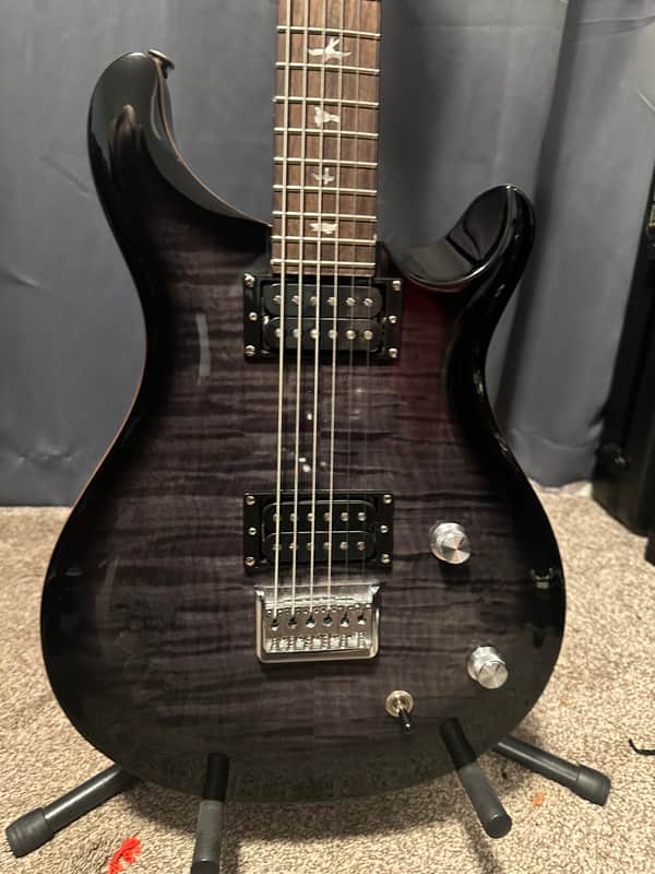 Black electric guitar hanging on a white wall.