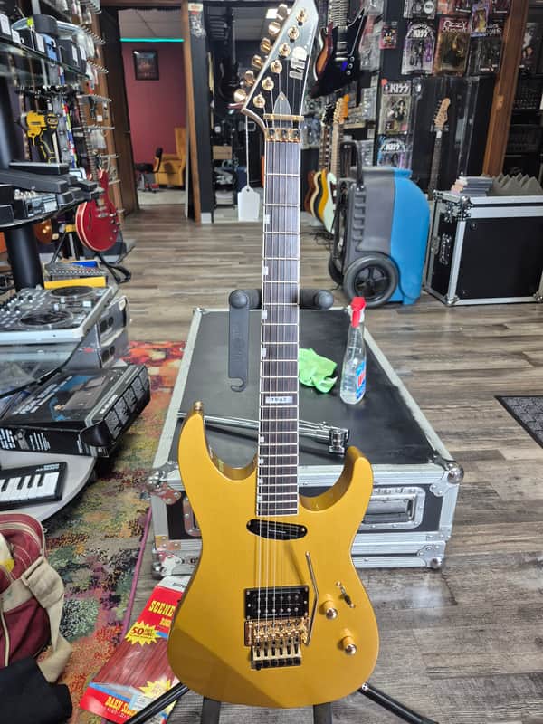 Gold electric guitar with black pickguard and hardware, displayed on red fabric.
