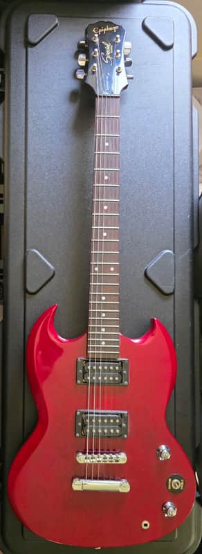 Red electric guitar on stand, black hardware, displayed against a white wall.