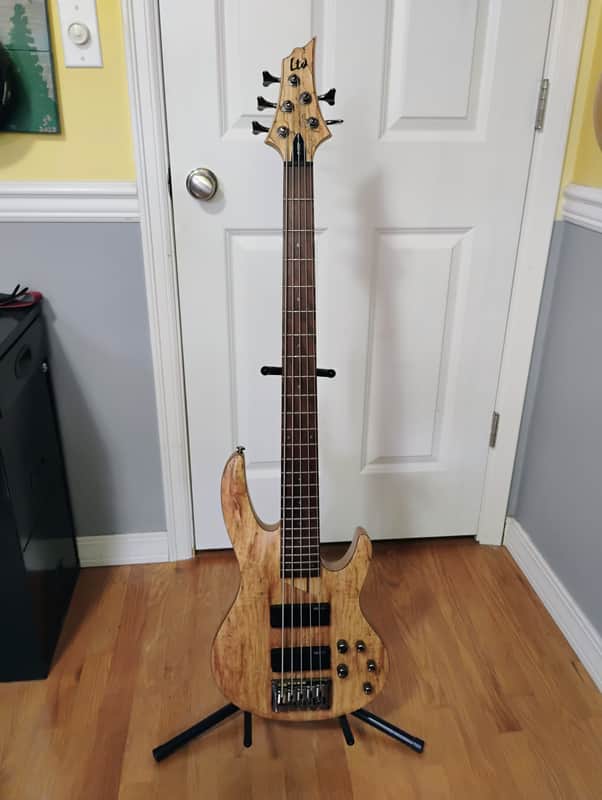 Dark, distressed electric bass guitar standing upright on a wooden floor.