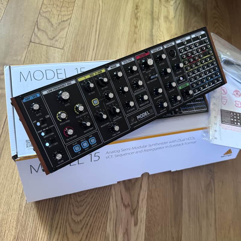 Black mixing console with numerous knobs and faders on a wooden surface.