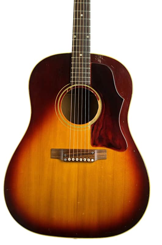 Acoustic guitar, sunburst finish, displayed vertically on a wooden floor.