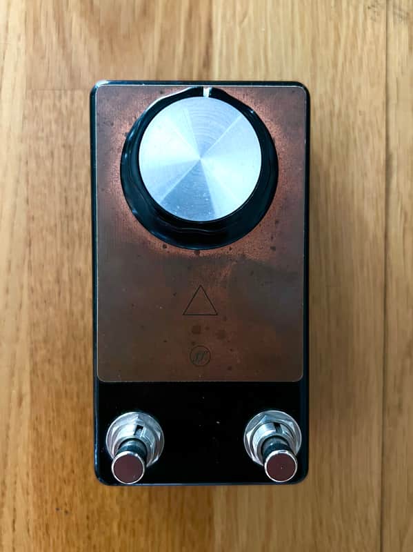 White box with barcode next to a small, gold and black electronic pedal.