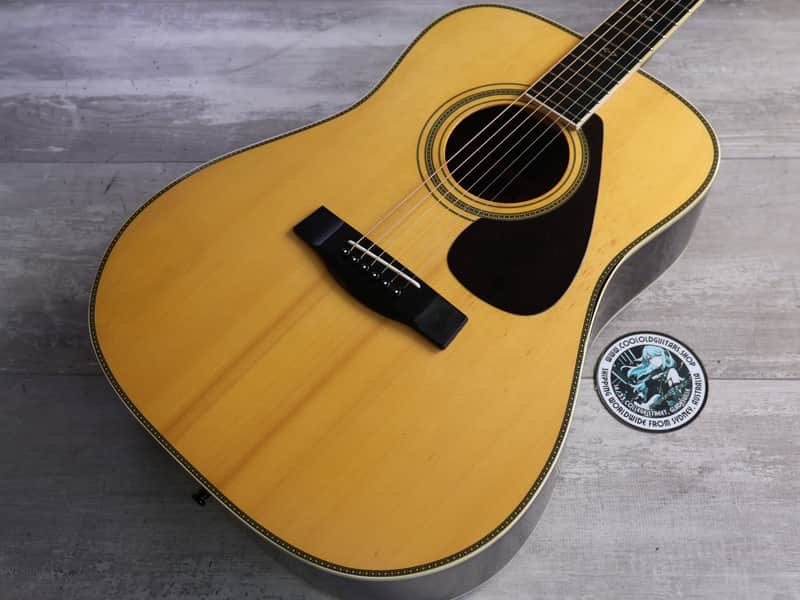 A natural wood acoustic guitar with a black pickguard, displayed upright.