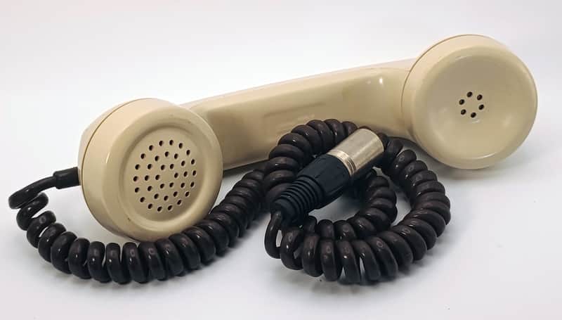 Vintage beige and black rotary telephone with coiled cord.