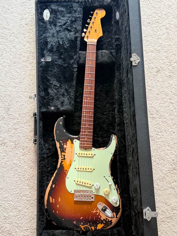 White electric guitar with brown body accents, resting in a yellow case.