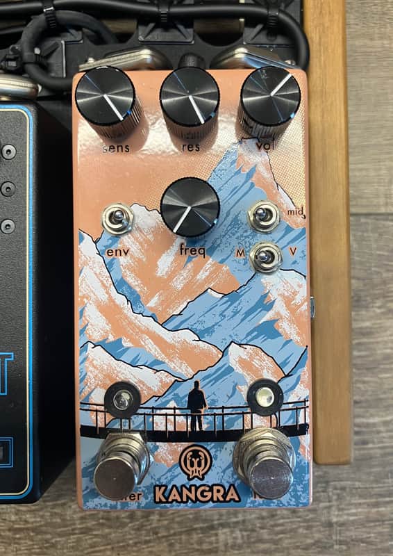 Orange guitar effects pedal with knobs, featuring a mountain landscape graphic.