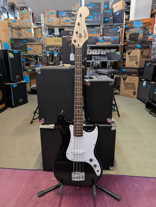 Black and white electric guitar on stand, natural wood neck, visible hardware.