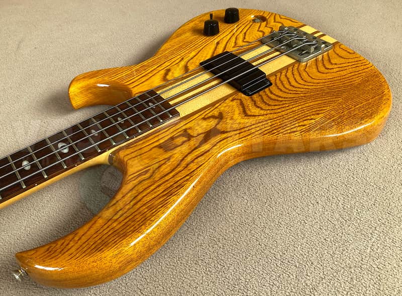 Brown electric bass guitar with black hardware, resting on black textured surface.