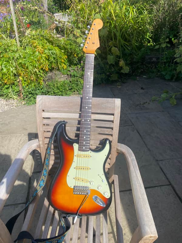 Red electric guitar with white pickguard, visible hardware, on a wooden surface.