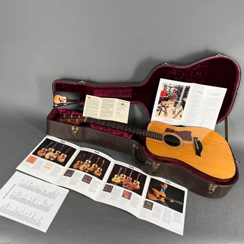 Taylor acoustic guitar, natural wood finish, displayed on stand.