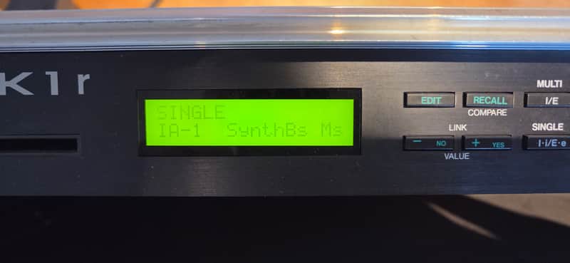Black digital synthesizer module with illuminated yellow display and various control buttons.