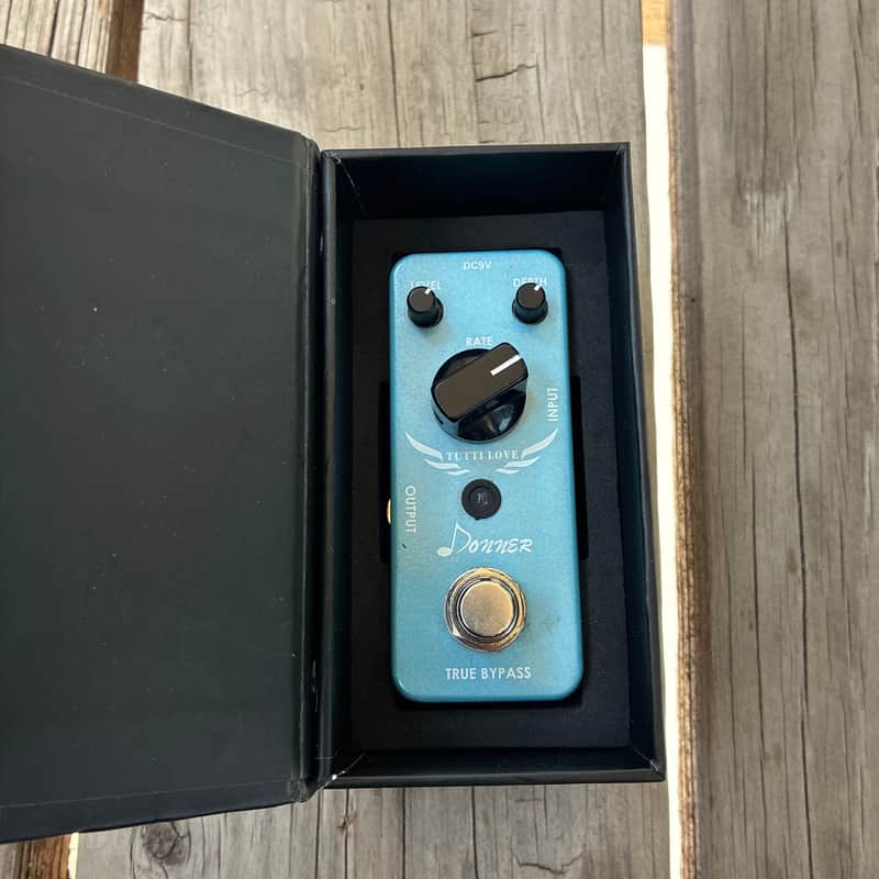 Blue and silver guitar effects pedal in original box. Knobs and switches visible.