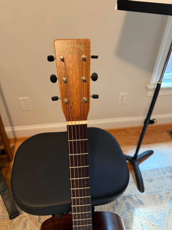 Dark brown acoustic guitar, visible soundhole, on black stand.