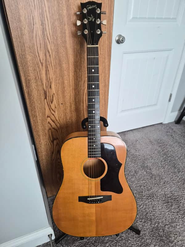 Vintage acoustic guitar, brown wood, displayed outdoors against a brick wall.