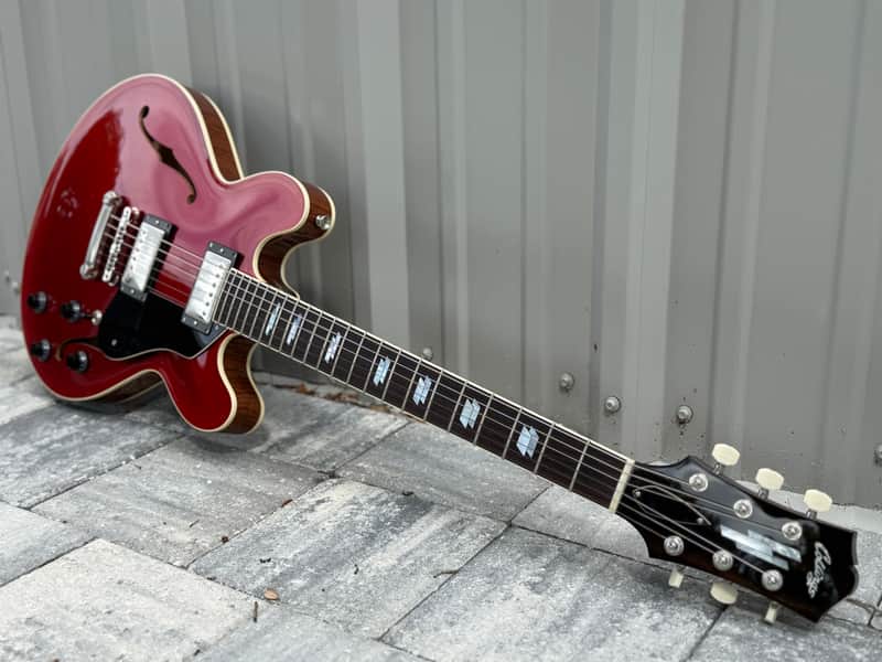 Red hollow-body electric guitar in open case, showing fretboard and hardware.