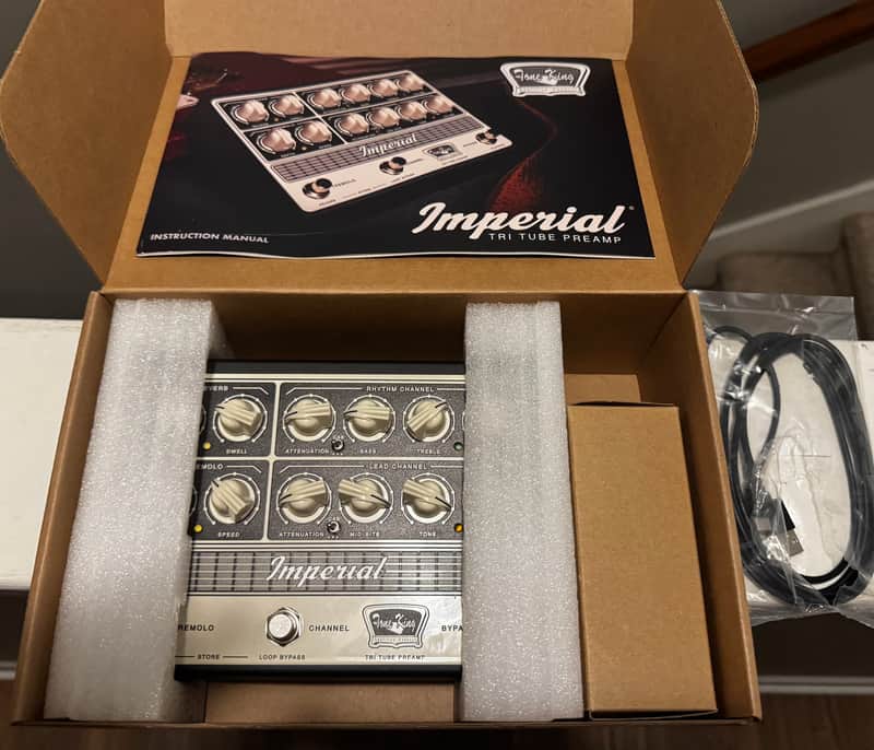 Black and silver tube preamplifier in open box with instruction manual.