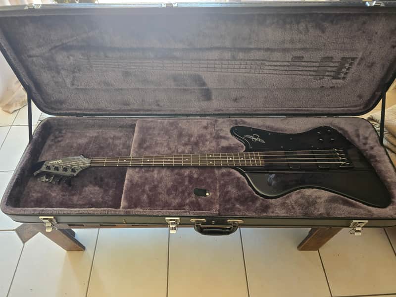 Brown and black electric guitar in open, grey velvet-lined carrying case.