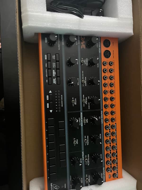 Black synthesizer keyboard with numerous knobs and pads on a countertop.