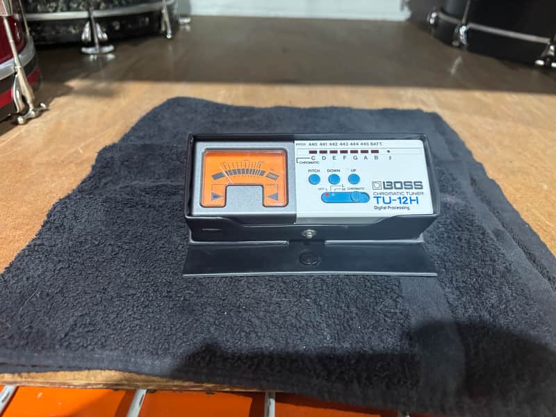 Black electronic tuner device resting on a colorful patterned rug.