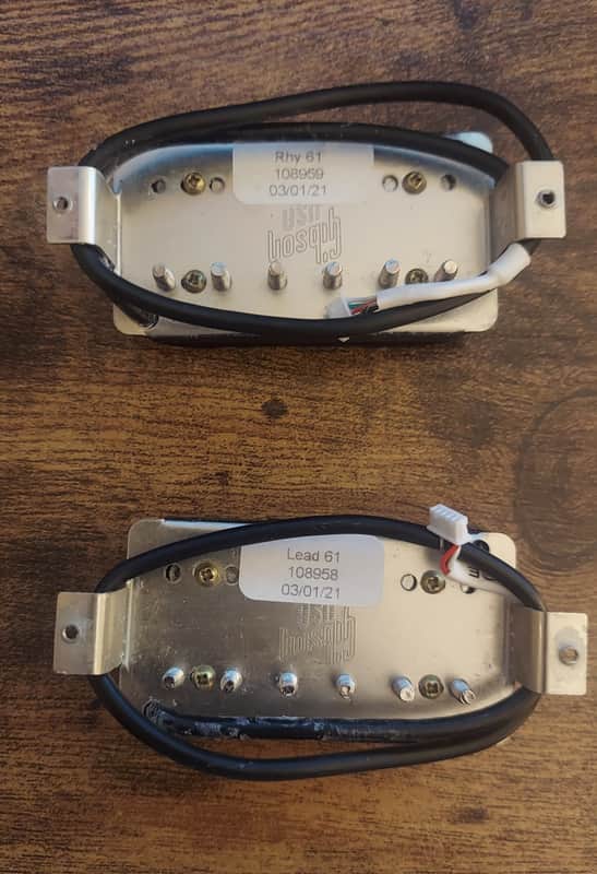Two black guitar pickups with chrome hardware, mounted on a metal bracket.