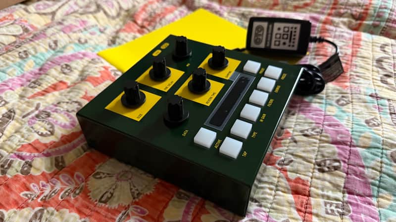 Green guitar effects pedal with black knobs, connected to a clear effects box.