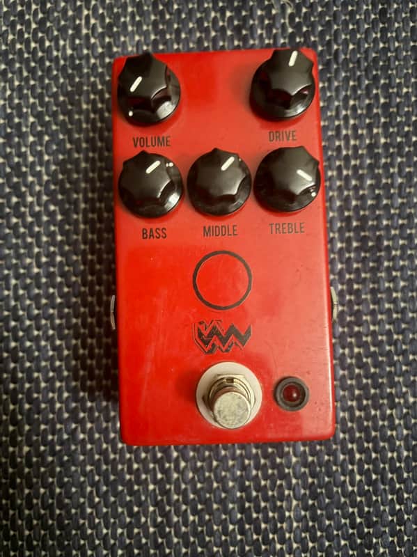 Red guitar amplifier with knobs, sitting on weathered wooden planks outdoors.