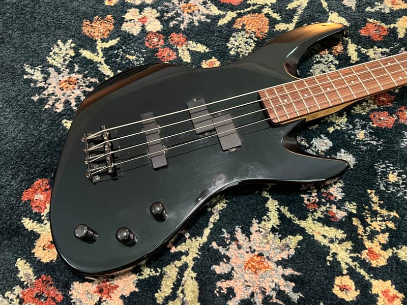 Red electric bass guitar, glossy finish, resting on a textured green surface.