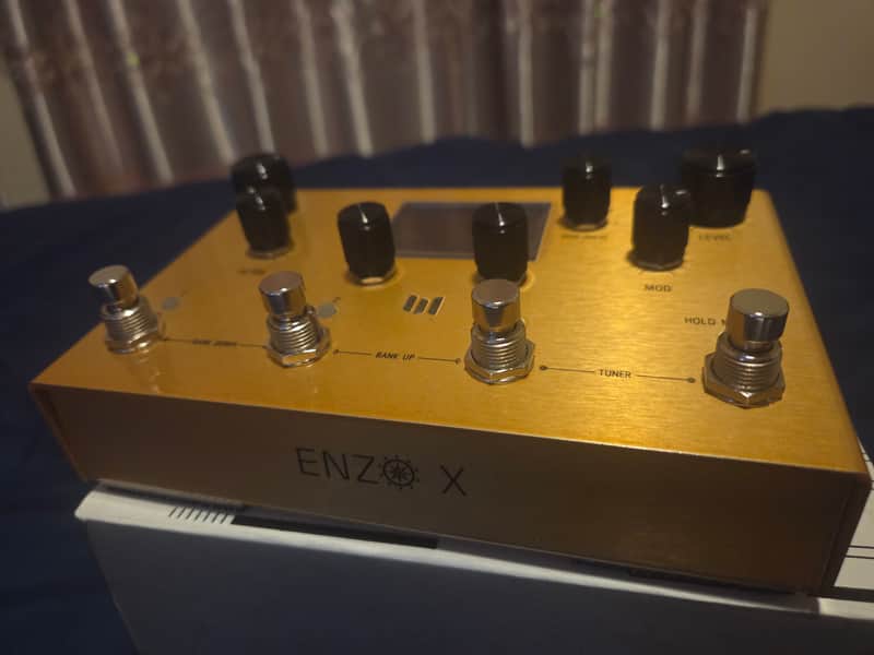 Gold-colored electronic effects pedal with knobs and central display.