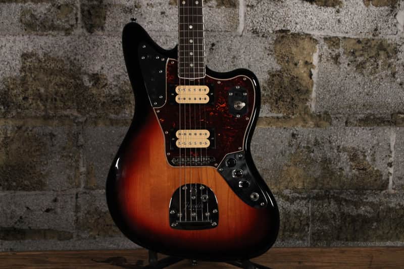 Sunburst electric guitar on stand, natural wood background.