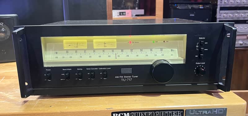 Black and silver stereo tuner with illuminated display and knobs.