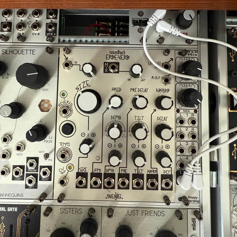 Black sound effects pedal with knobs and jacks, next to a white strap.