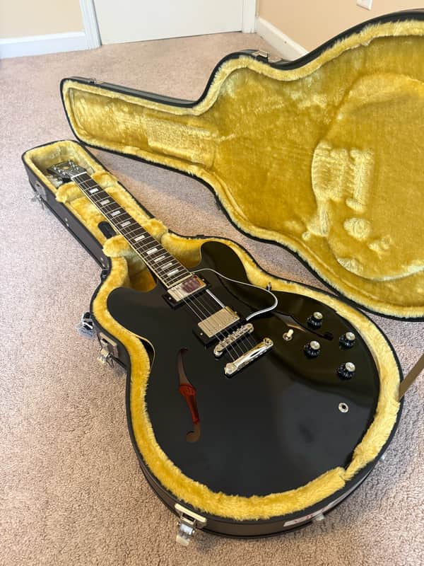 Solid red electric guitar with black hardware, resting on a patterned rug.